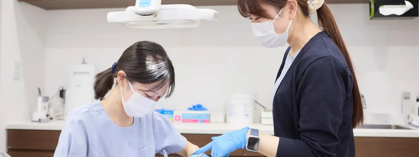 診療室で、先輩スタッフが後輩に手技を教える様子